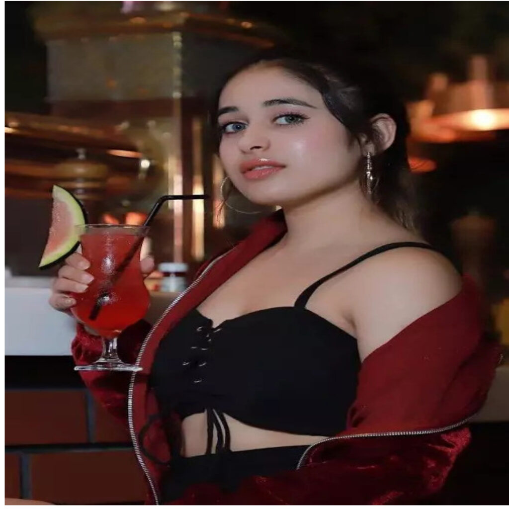 A GIRL 22 YEARS OLD NAME IS PREETI WEARING RED JACKET AND BLACK BIKINI TAKING ACLASS OF JUCE IN STANDING POSITION